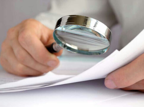 Person examining document with magnifying glass.