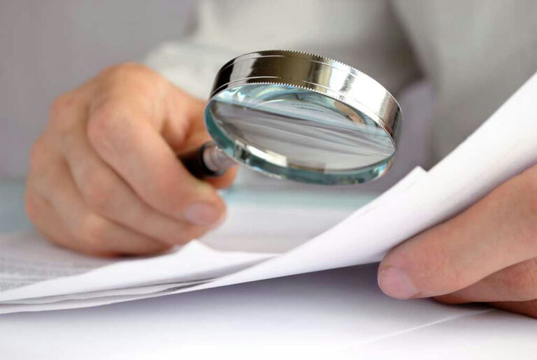 Person examining document with magnifying glass.