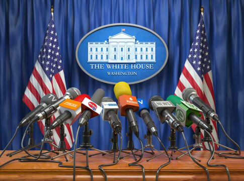 White House podium with multiple microphones and flags.