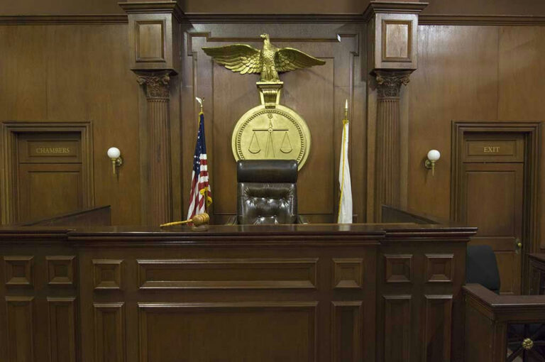 Judges bench in an empty courtroom, scales emblem above.