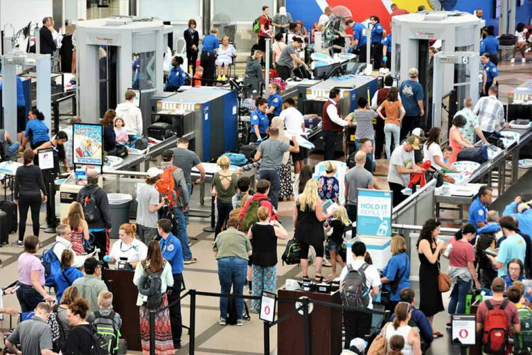 Crowd at an airport security checkpoint with TSA officers.