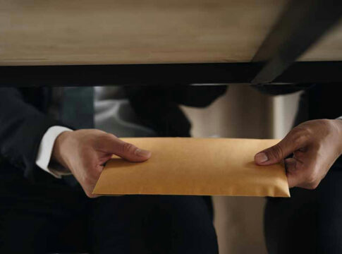 Two people exchanging an envelope under a table.