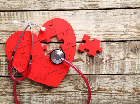Heart-shaped puzzle and stethoscope on wooden background.