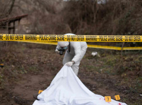 Police crime scene with investigator examining covered body