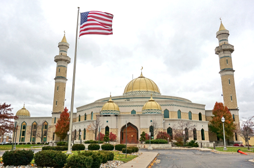 A mosque with a golden dome and minarets, featuring an American flag in front