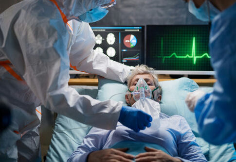 Patient on hospital bed with oxygen mask assisted by healthcare workers