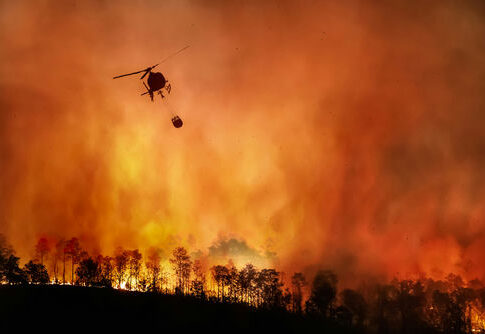 Helicopter dropping water on large forest fire.