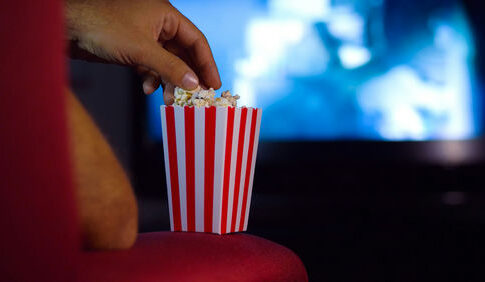 A hand reaching into a striped popcorn container while watching a movie