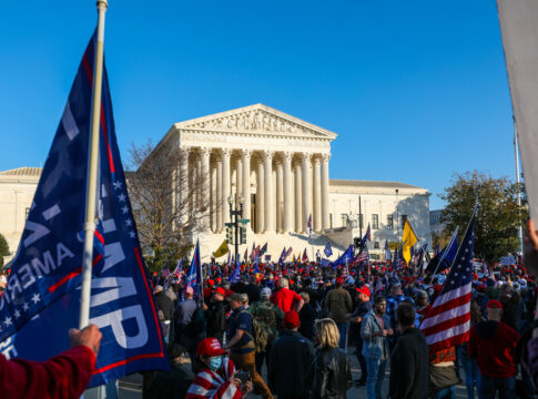 Crowd gathered outside large government building with flags