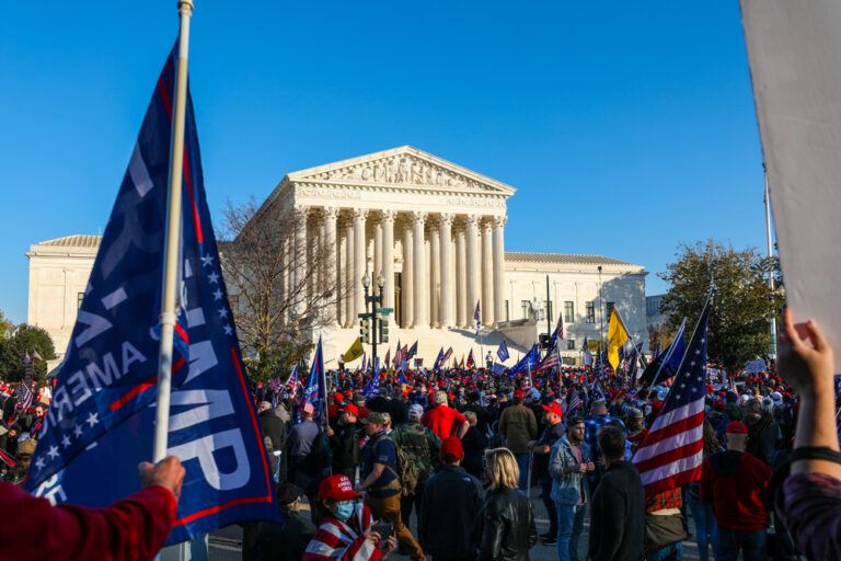 Crowd gathered outside large government building with flags