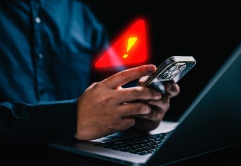 Person holding a smartphone with a notification alert while using a laptop