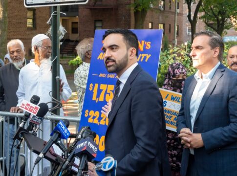 Man in suit speaks at outdoor press conference with microphones